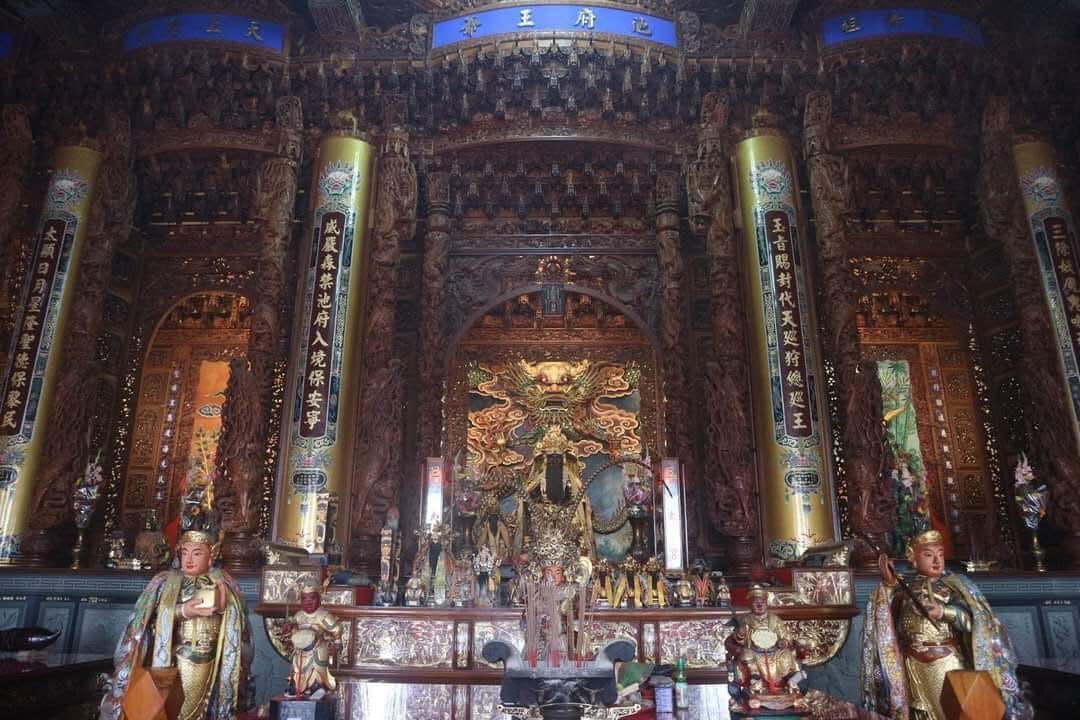 裝飾華麗的金色寺廟祭壇,中央供奉著神像,兩側是兩尊守護神像,周圍環繞著雕刻精美的柱子和燈盞。