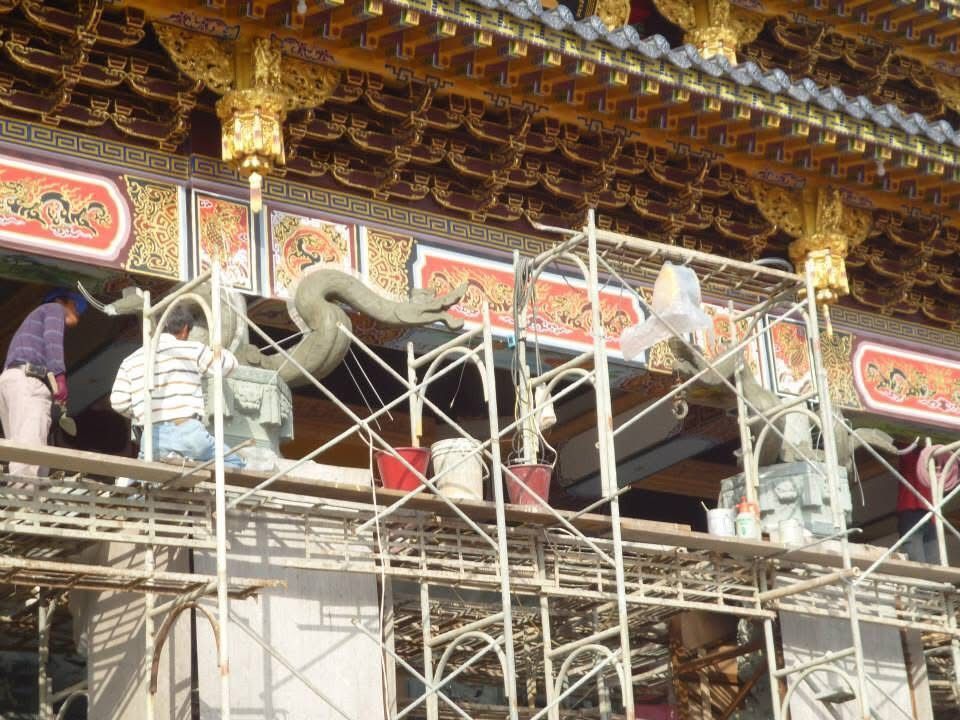工人們在鷹架上修復裝飾華麗的寺廟屋頂,屋頂上雕刻著龍形圖案並飾有金色細節。