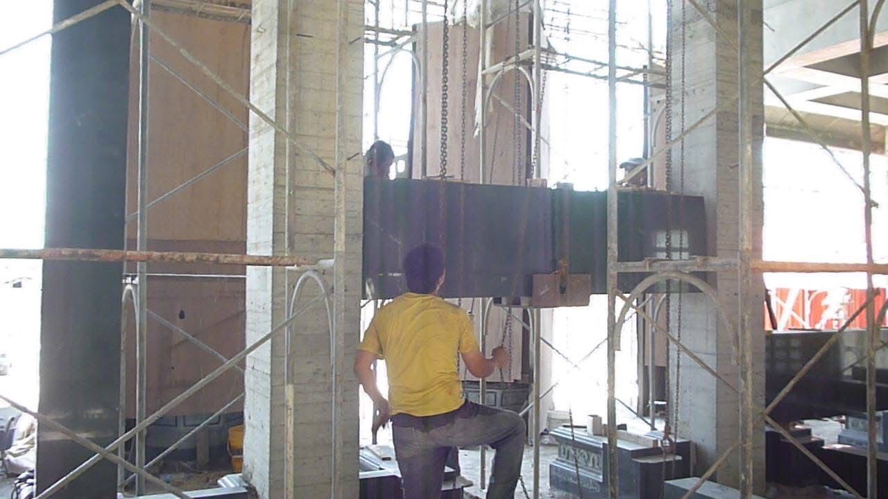 一名身穿黃色襯衫的工人站在鷹架搭建的建築工地上,旁邊是巨大的混凝土柱子。