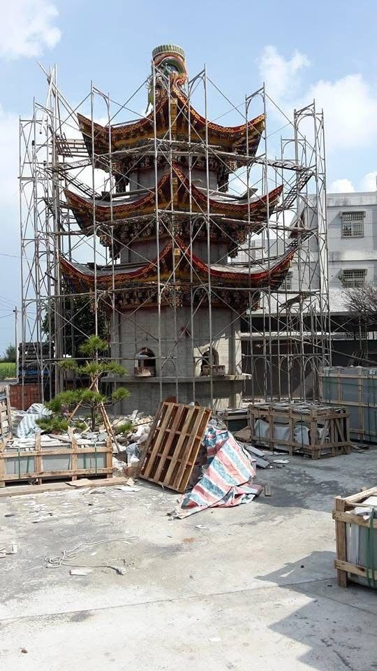 混凝土庭院內,一座多層寶塔正在施工,鷹架和建築材料散落在庭院中。