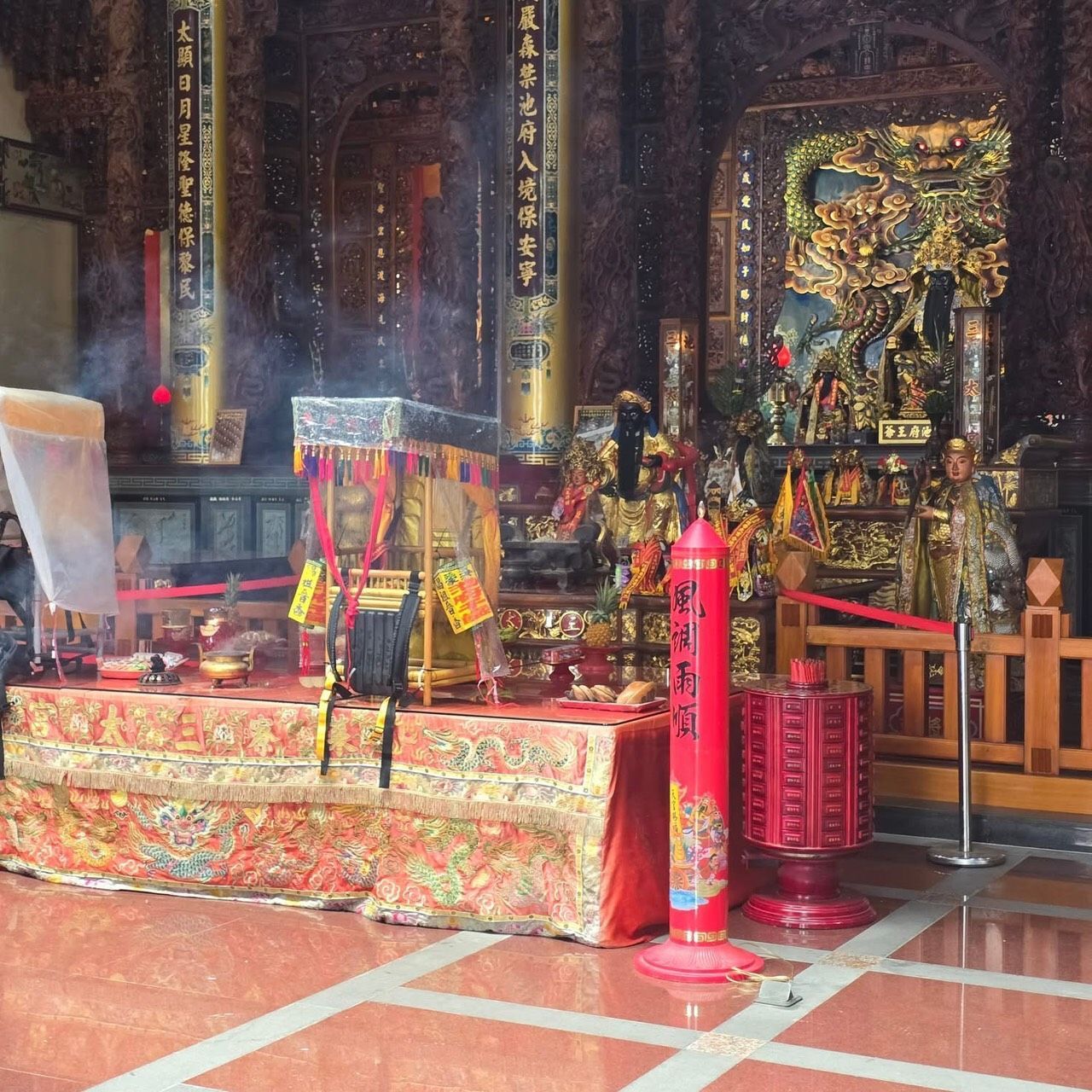 裝飾華麗的寺廟祭壇,擺放著紅色供台、花紋布幔,背景矗立著一尊金色神像。