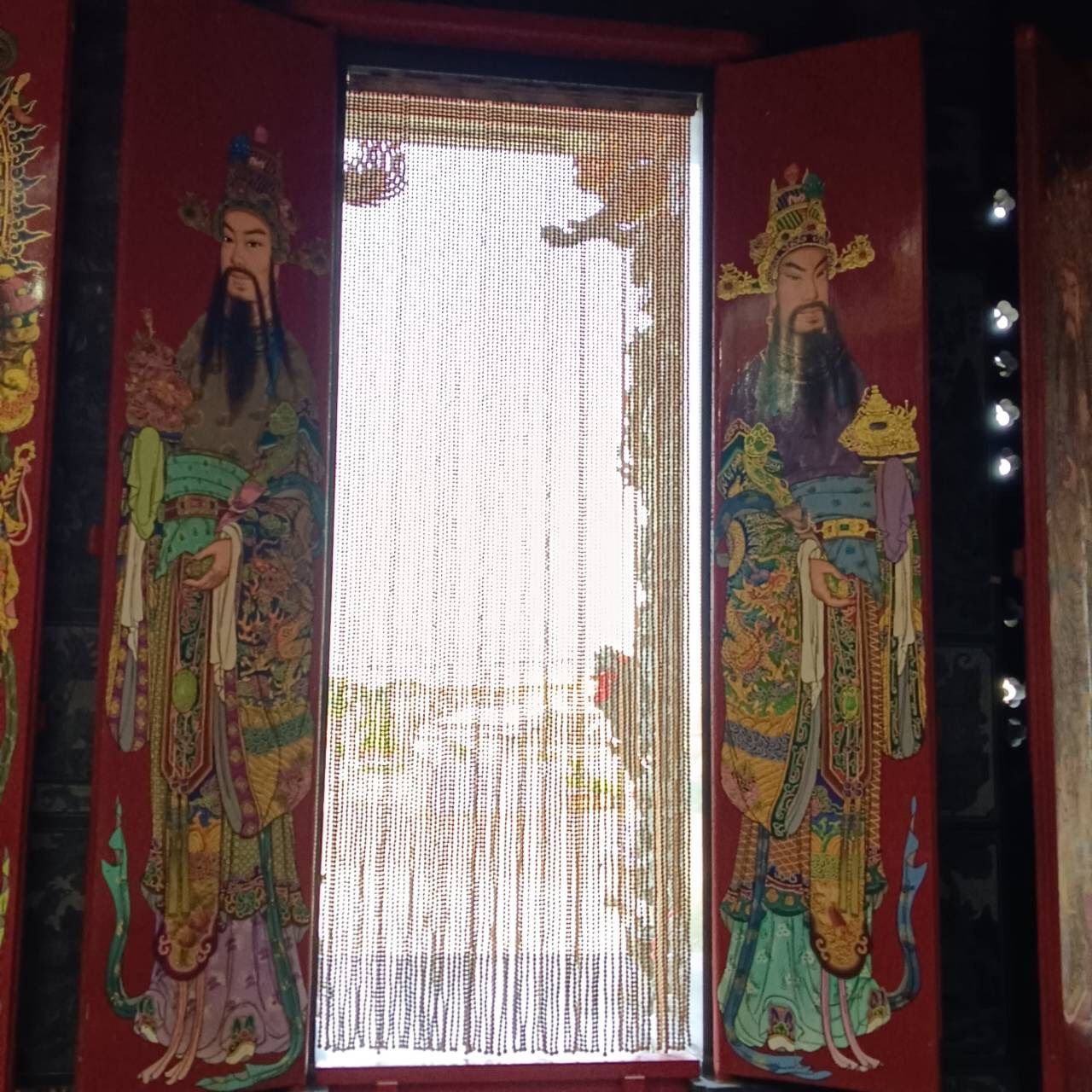 裝飾性的門廊,紅色面板上繪有人物圖案,珠簾在日光下熠熠生輝。