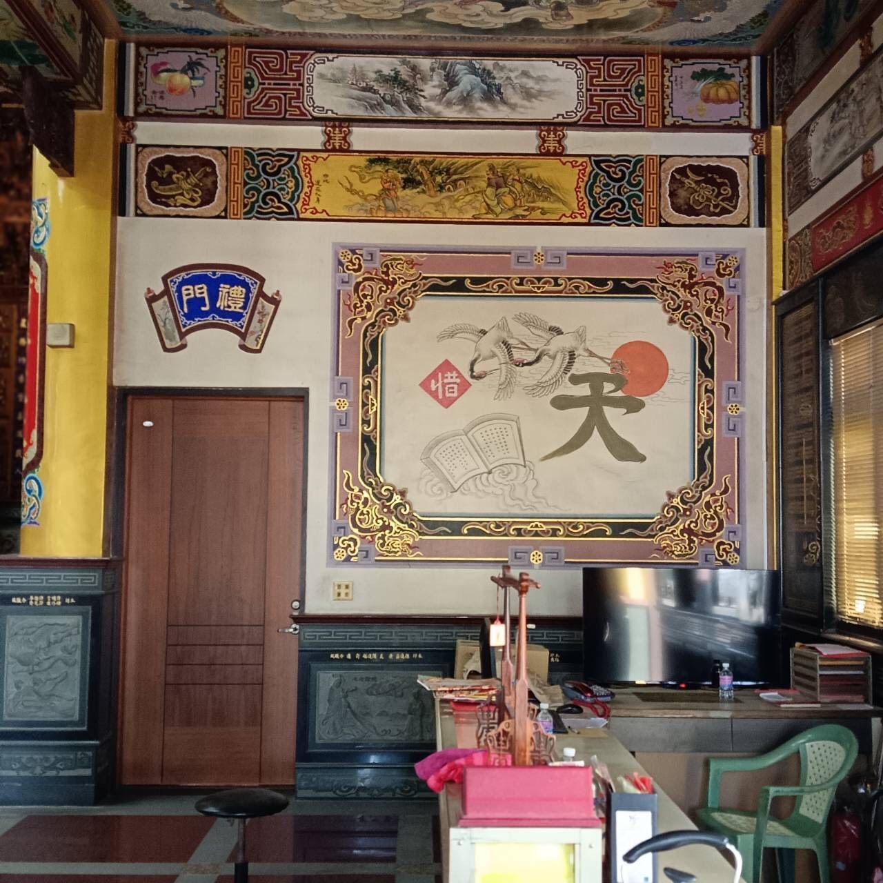 房間裝潢華麗,牆上掛著中式藝術品,配有木門、電視和綠色椅子,營造出溫馨的氛圍。