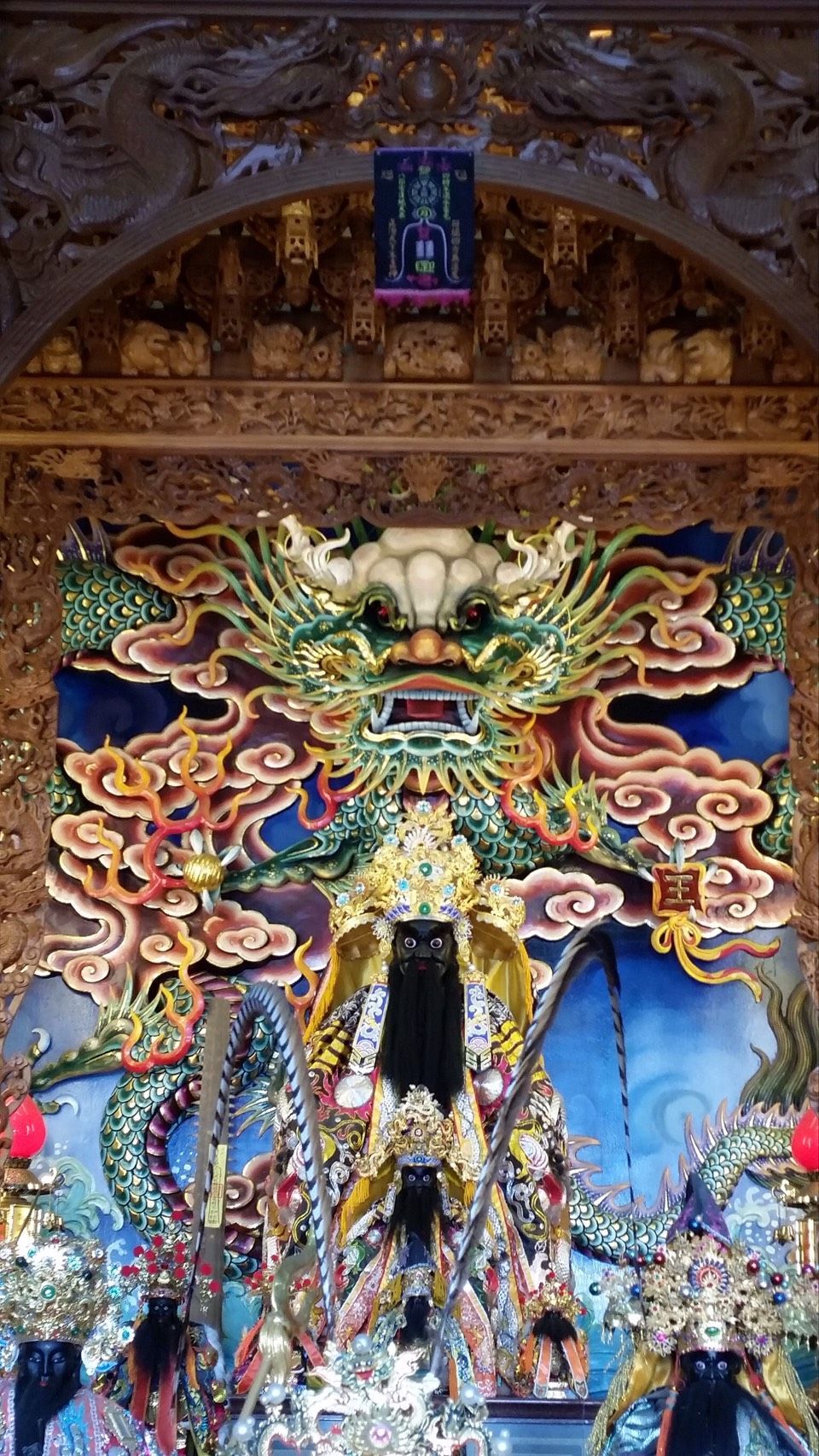 寺廟祭壇上方繪有色彩繽紛、裝飾華麗的龍形壁畫,綠色、紅色和金色交織纏繞,細節精美。