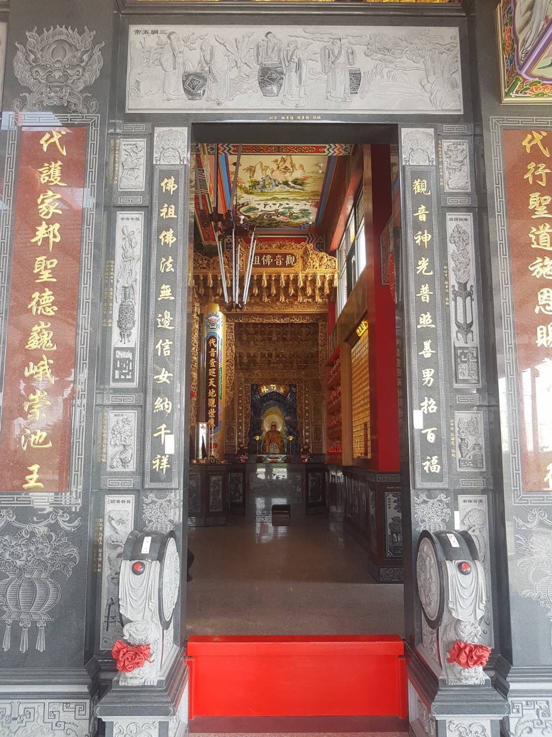 寺廟入口處有精美的雕花門廊、紅色台階和金色的中國書法裝飾板。