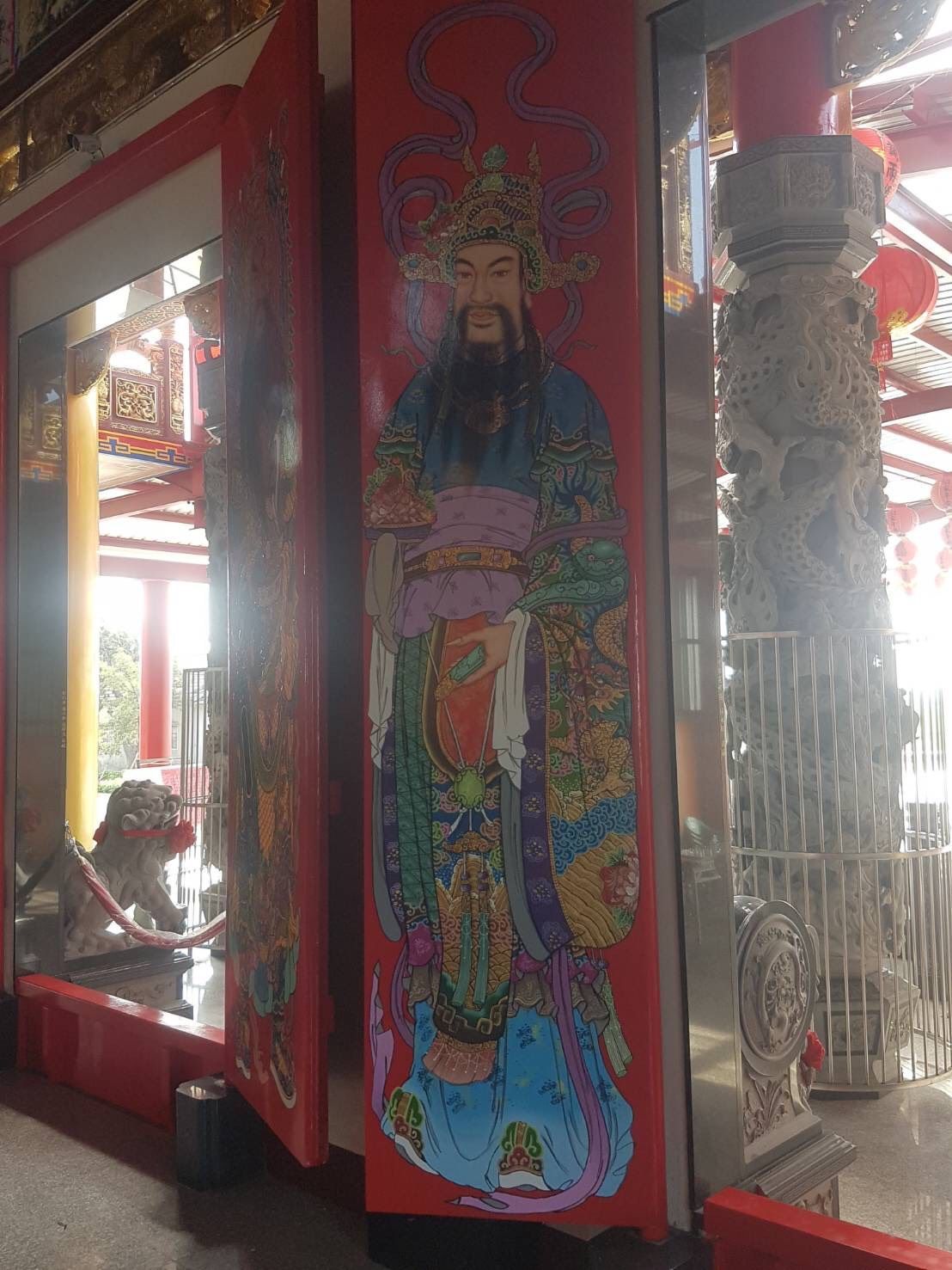 寺廟走廊,紅色柱子旁繪有色彩鮮豔的壁畫,描繪了一位留著鬍鬚的神祇,並懸掛著燈籠。
