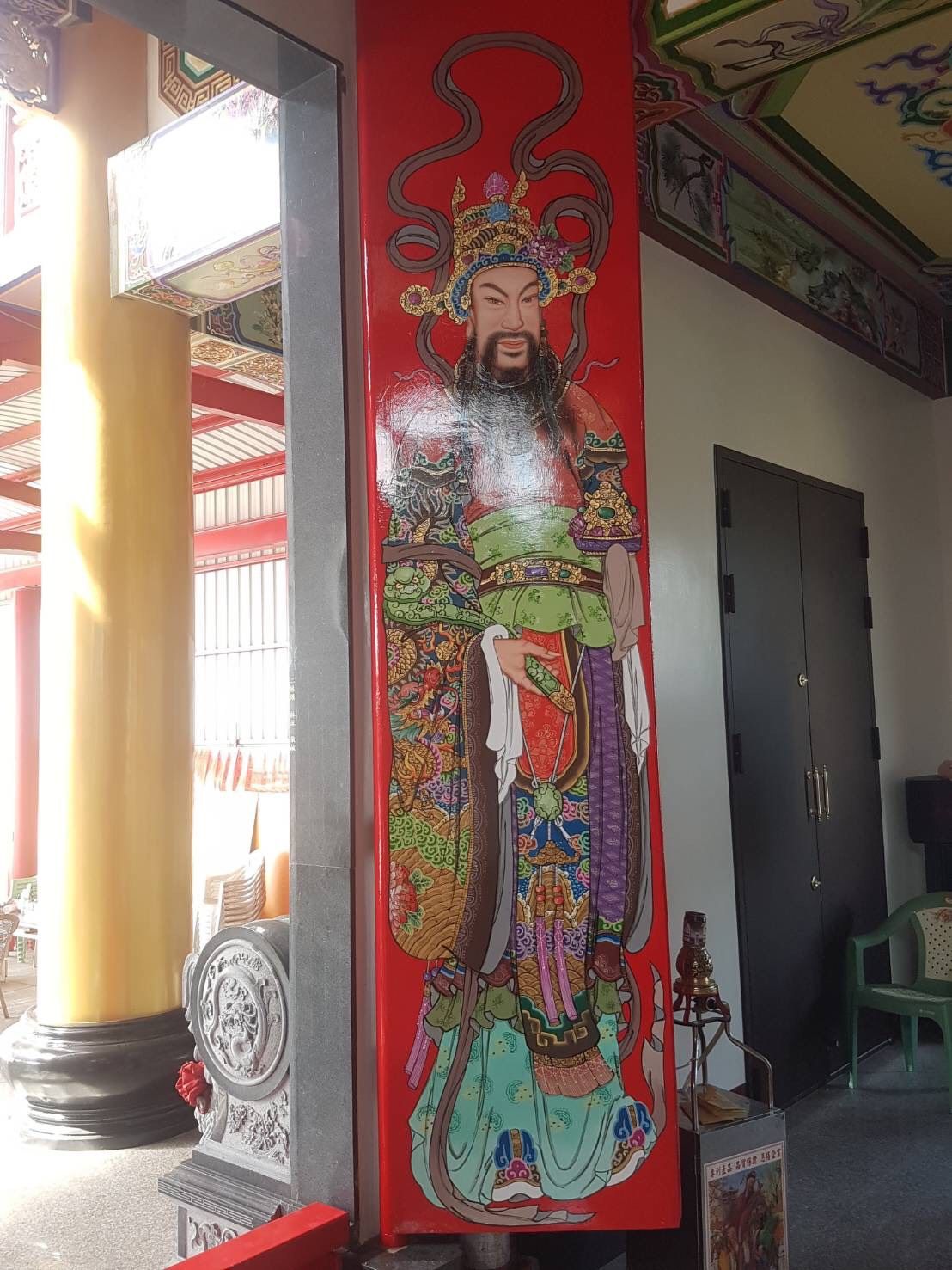 在寺廟般的走廊內,一根紅色柱子上繪有高大的彩色神像壁畫。