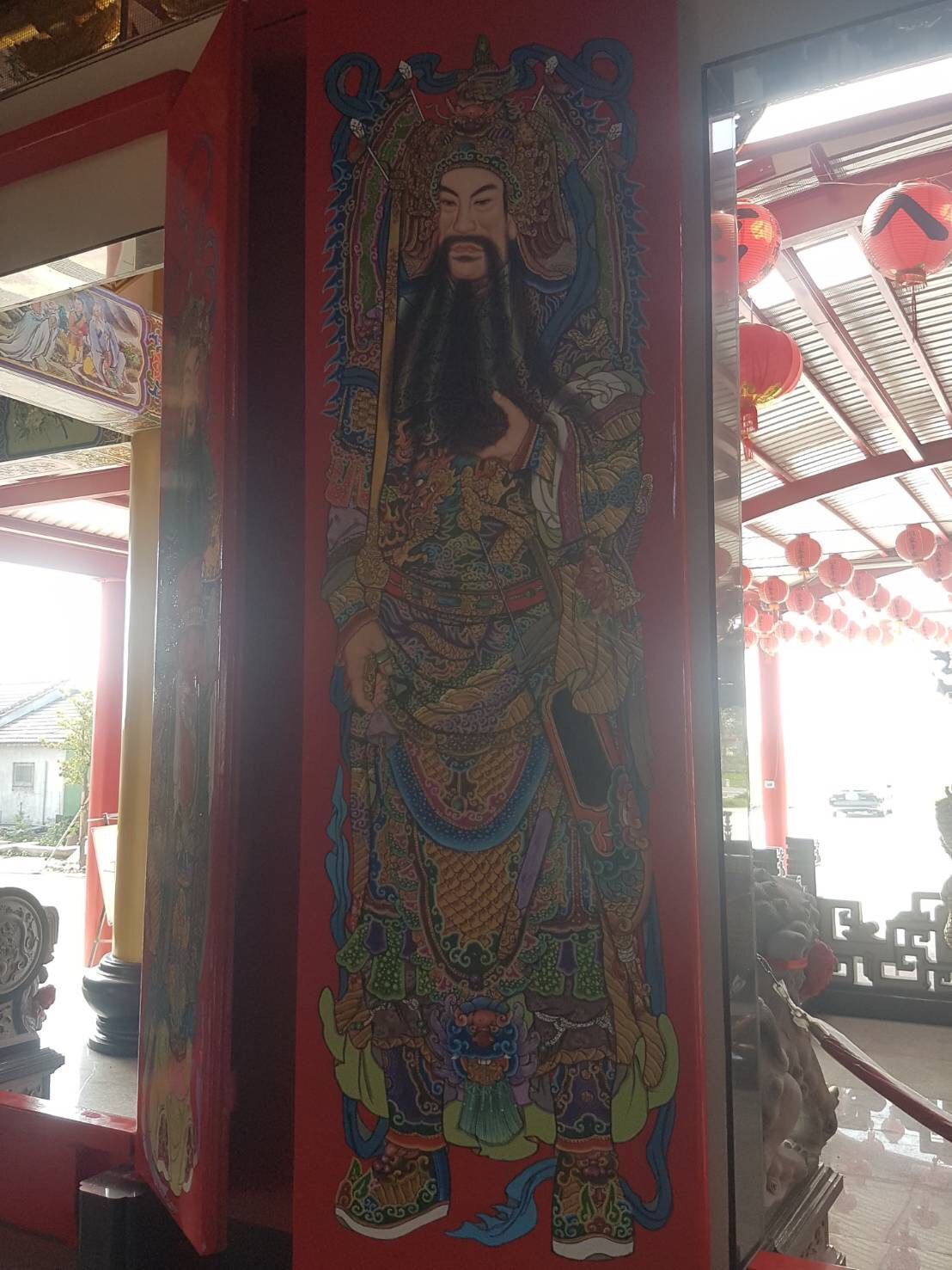 紅色寺廟或亭台入口處,繪有一幅高大、色彩繽紛的壁畫,描繪的是一位蓄須神祇。