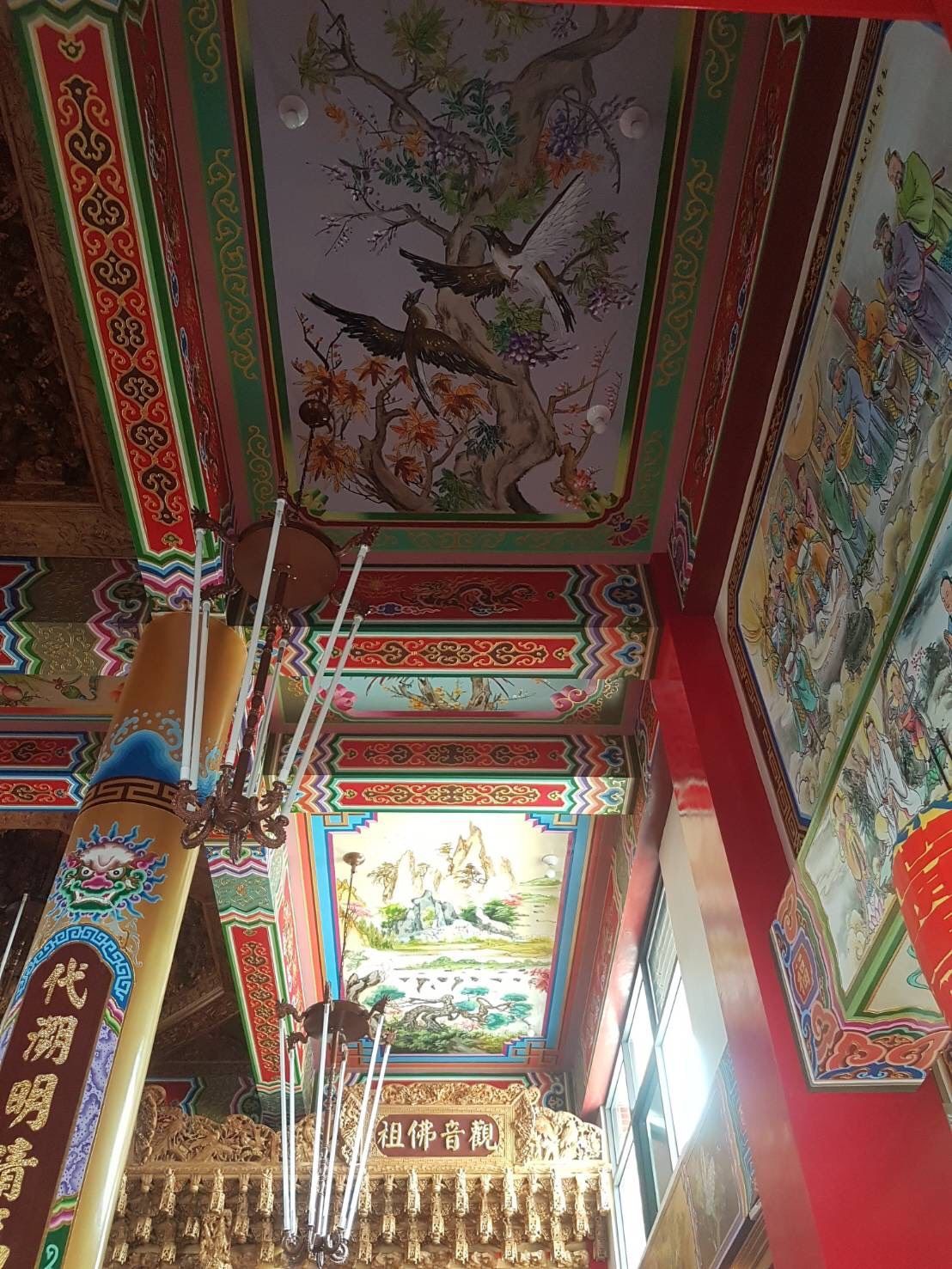 寺廟內狹窄的走廊,色彩繽紛的天花板上裝飾著華麗的紅色立柱、彩繪鑲板和懸掛的燈具。