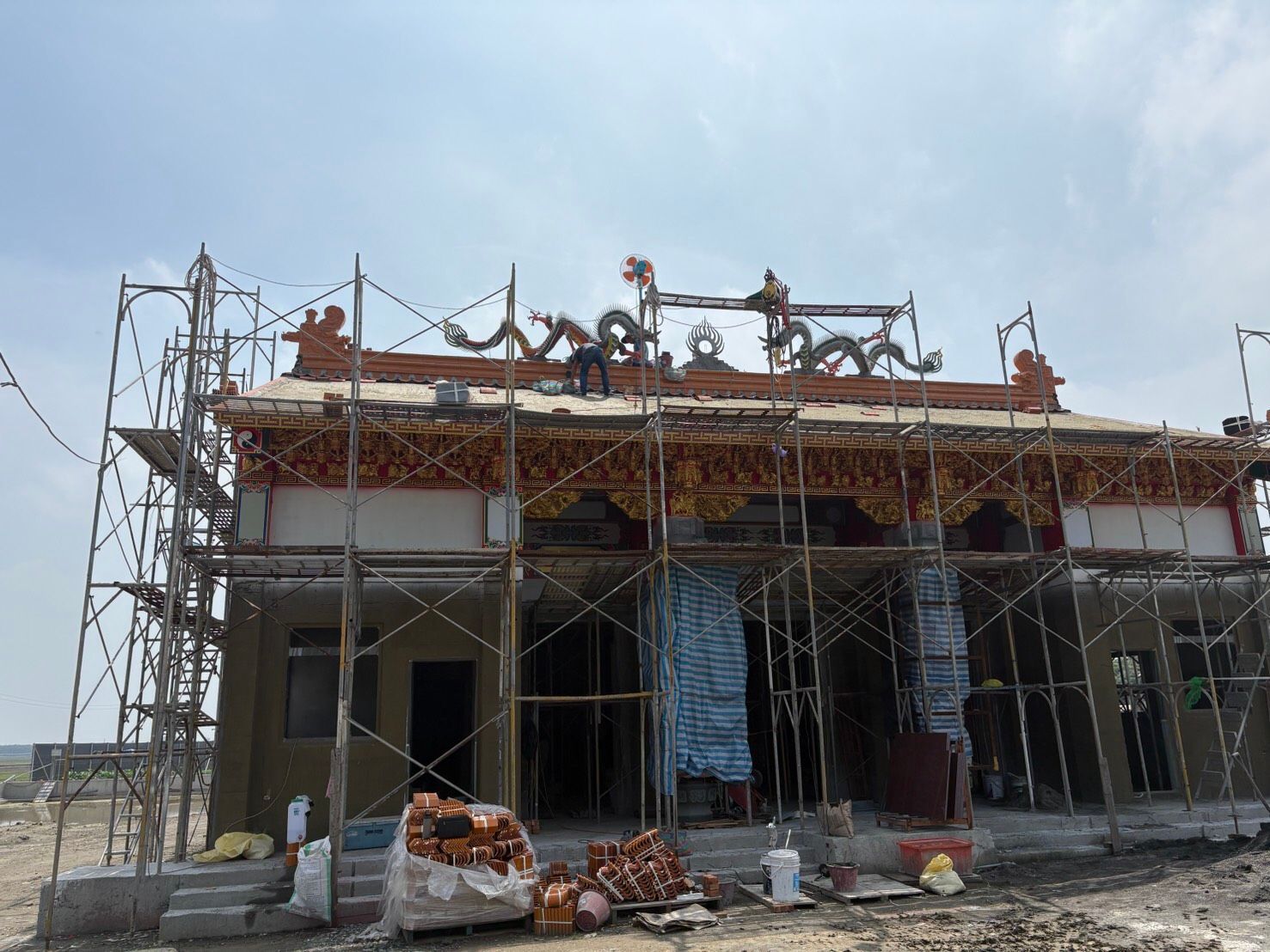 施工現場的建築物周圍搭起了鷹架,屋頂上有工人在作業,下面是建築垃圾。