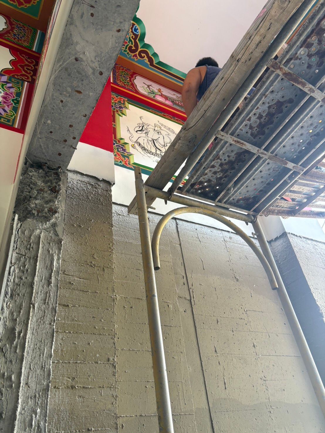 一個人站在裝飾性建築立面旁的金屬鷹架上,建築立面飾有紅色、綠色和金色的邊飾。