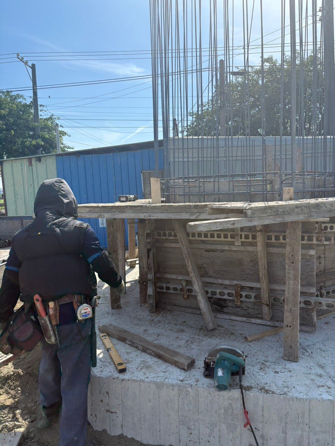 一名工人在建築工地上,旁邊是混凝土模板和垂直的鋼筋,地上散落著工具。