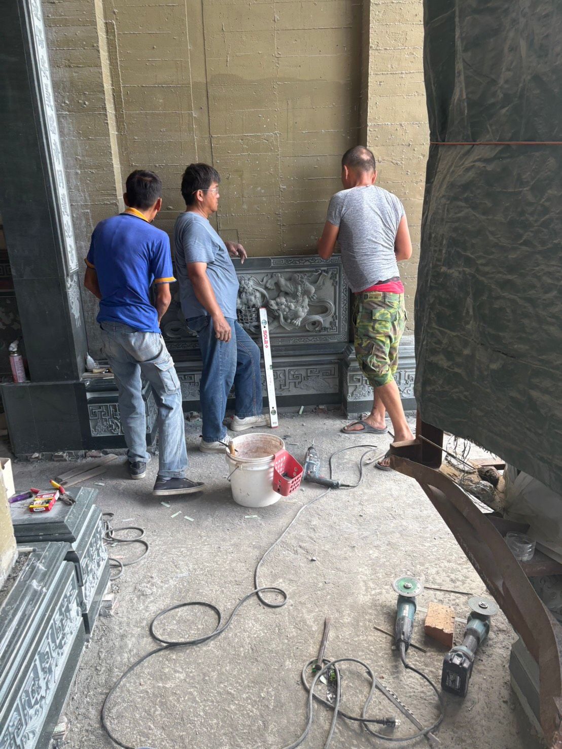三名工人在建築工地安裝牆磚,工具和材料散落一地。