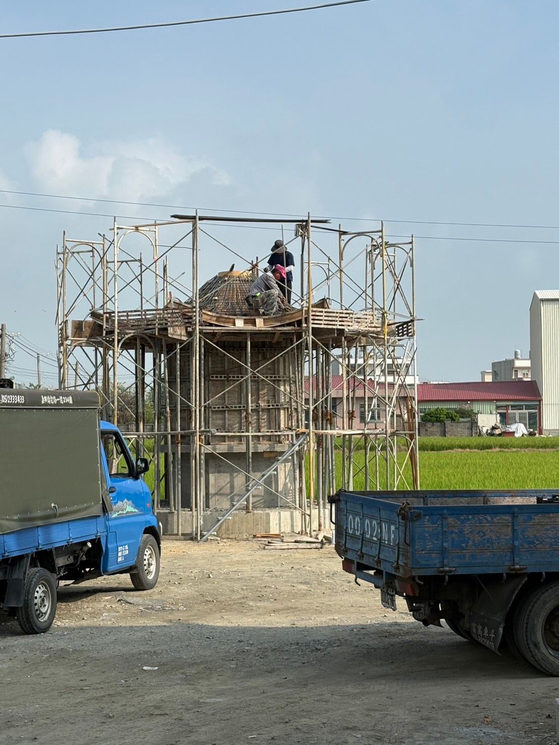 施工現場的建築物周圍搭起了施工鷹架,工人在上面作業,前面停著卡車。