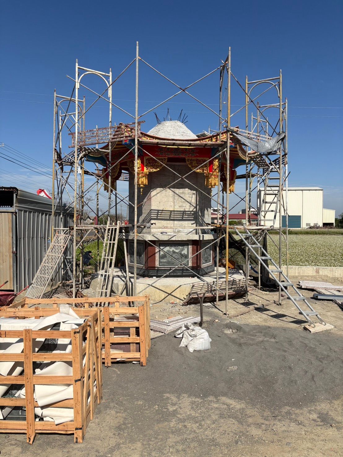 在陽光明媚的日子裡,一棟正在施工的小樓周圍搭起了鷹架,前景中可以看到一些托盤。