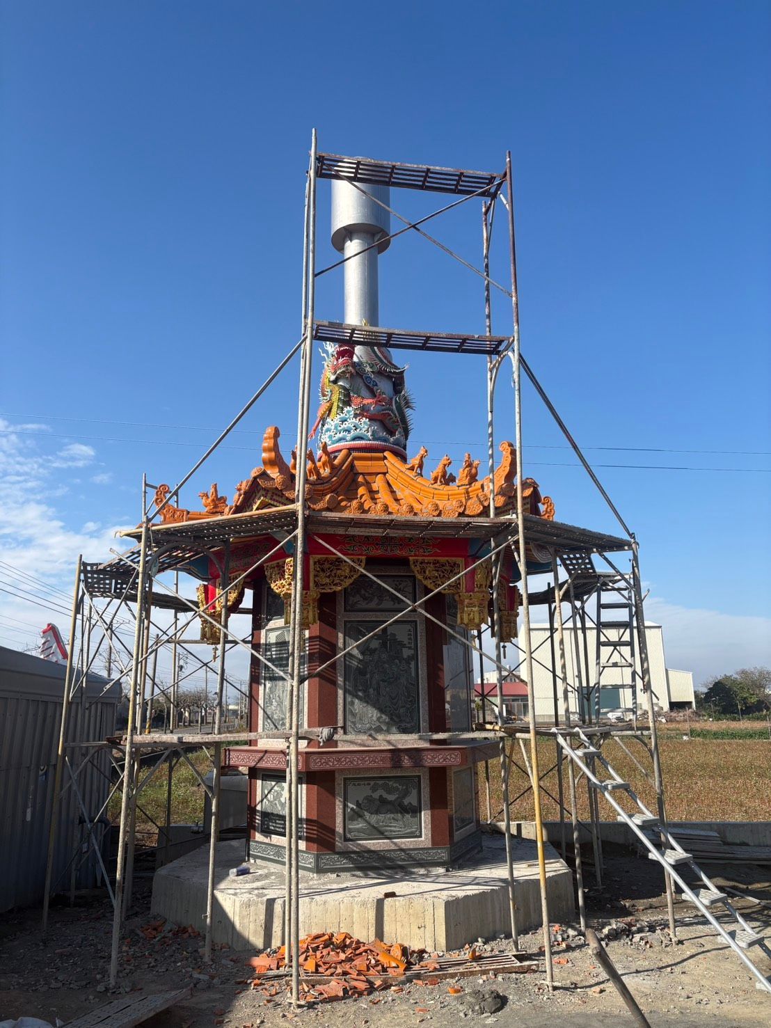 一座正在建造中的小型精美神龕或紀念碑,周圍搭滿了腳手架,天空湛藍如洗。