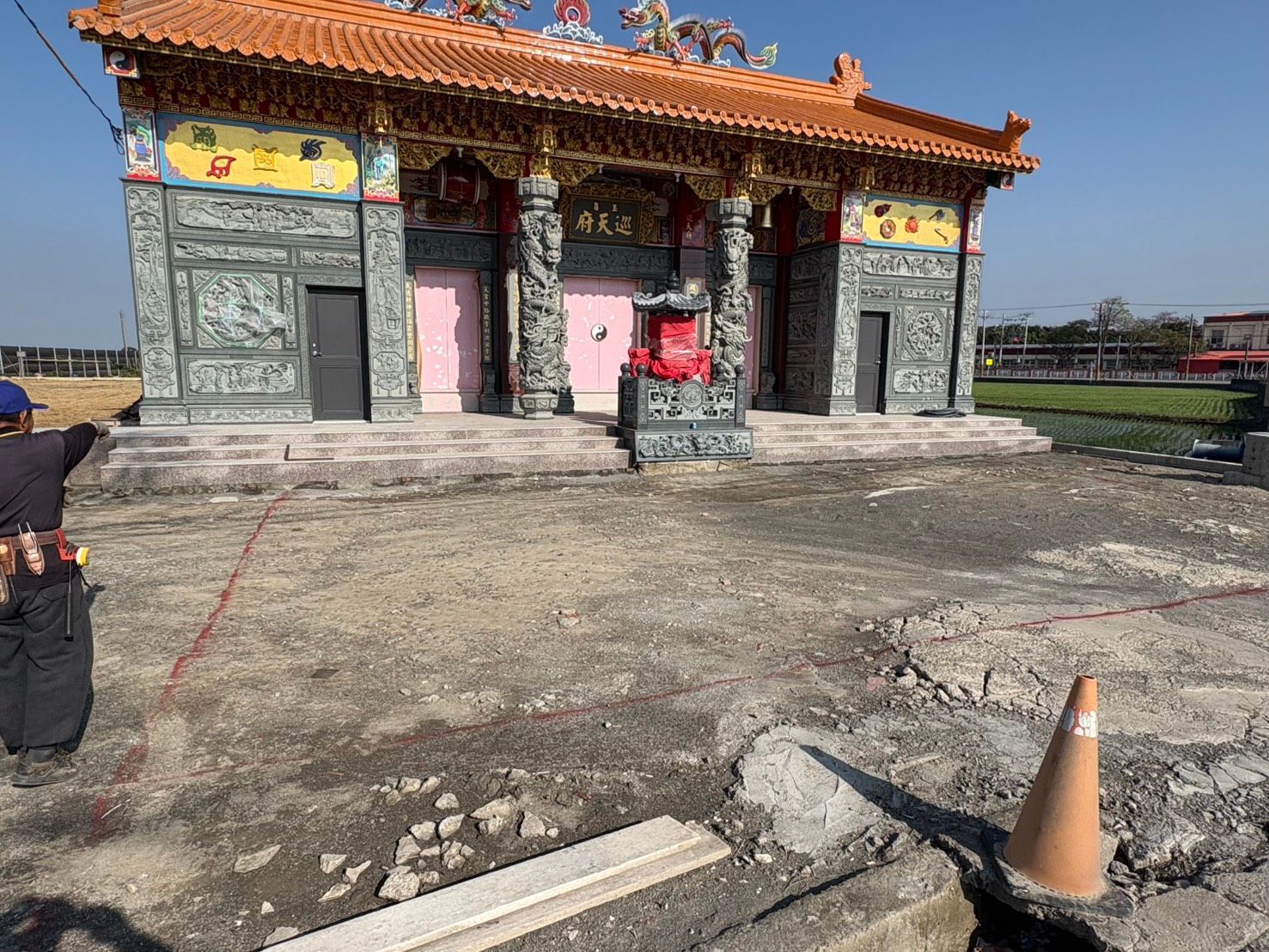 傳統寺廟建築,屋頂裝飾華麗,石砌庭院,前景可見交通錐。