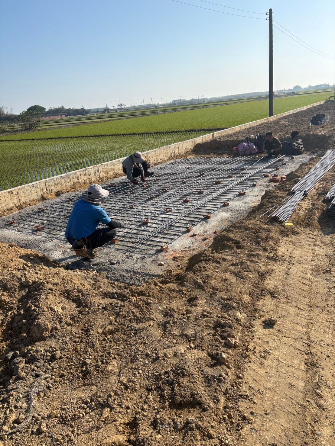 晴空萬裡,工人在鄉村公路旁綠油油的田野邊鋪設碎石。