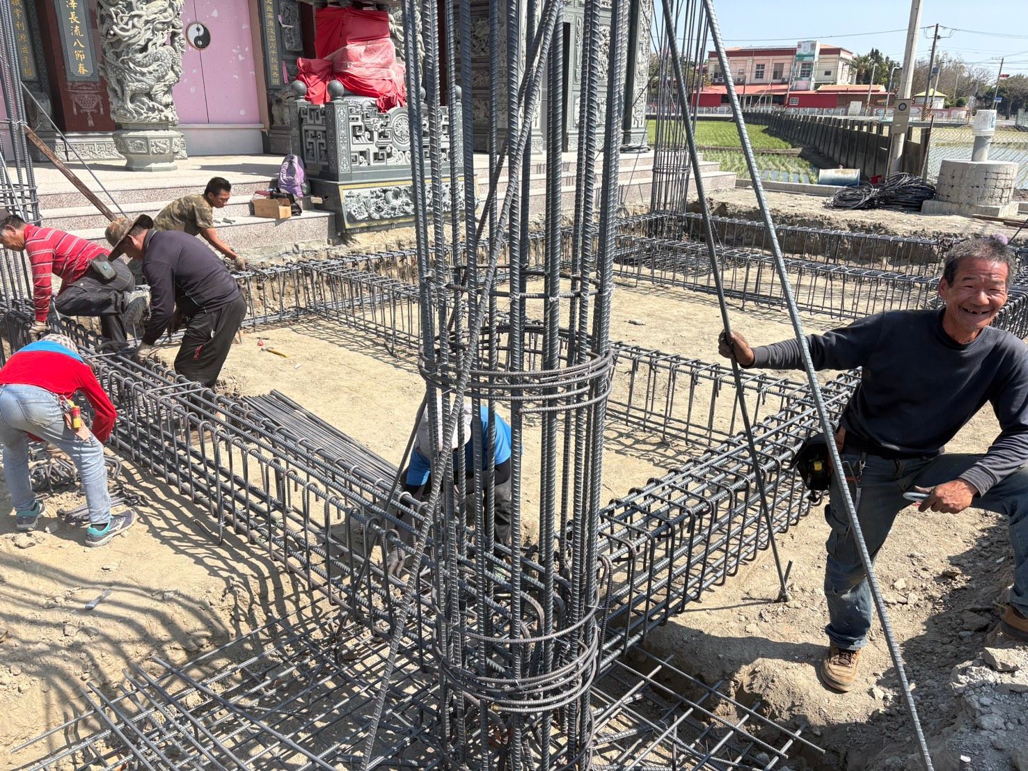 工人們正在建築工地安裝鋼筋地基,現場有鋼柱和泥濘的地面。