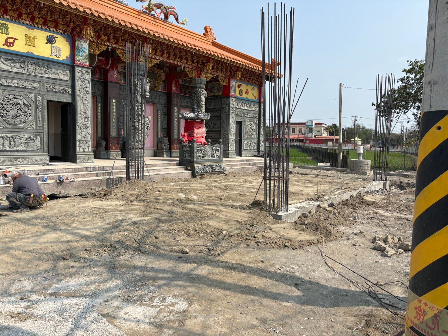 寺廟建築正在施工中,裝飾精美的石砌外牆旁裸露著鋼筋,地面泥濘。