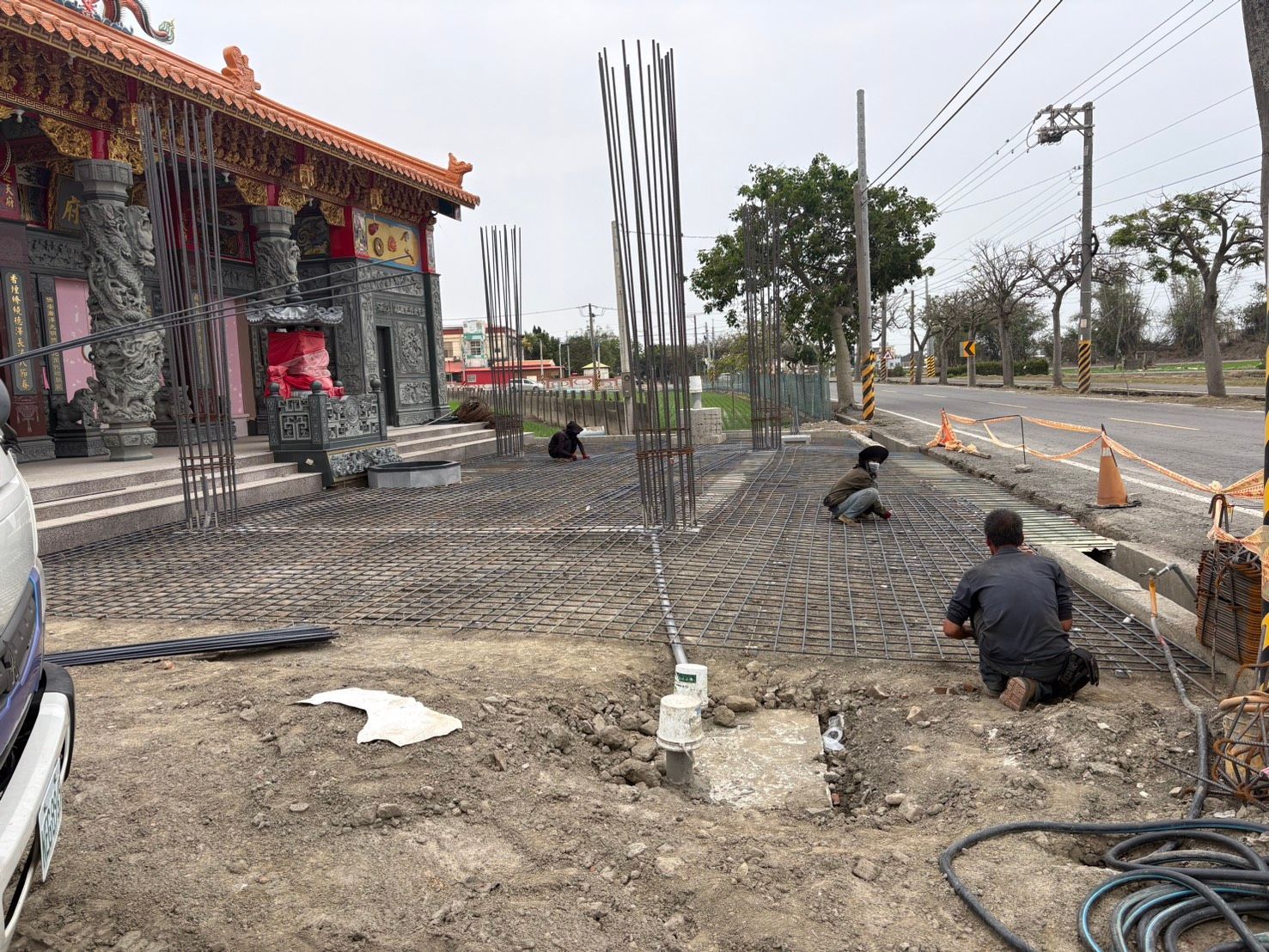 工人們正在寺廟旁平整土地,附近有鋼筋和道路。