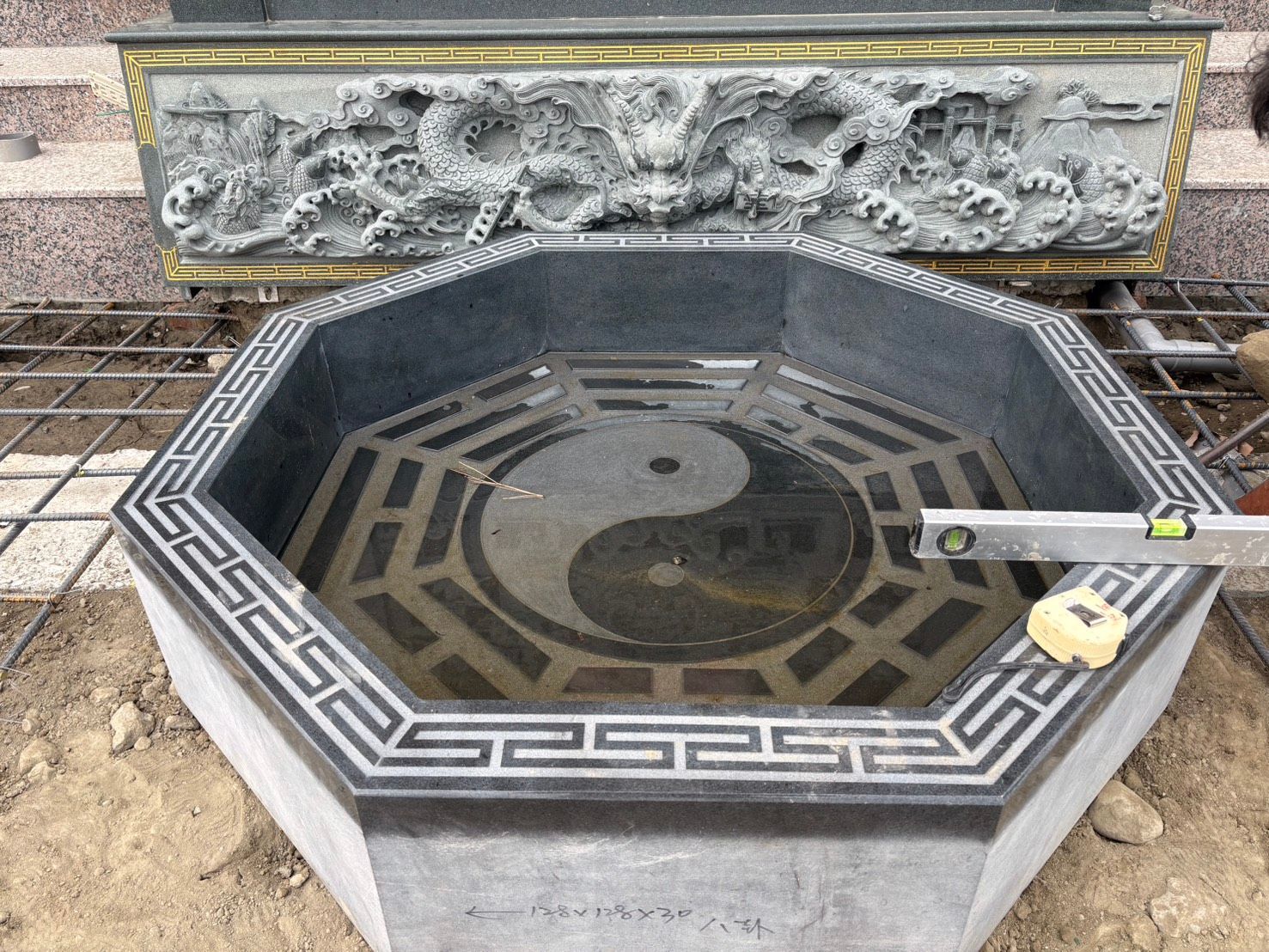 戶外設有陰陽圖案的八角形石質水池,旁邊是雕刻的石頭和鋪路石。