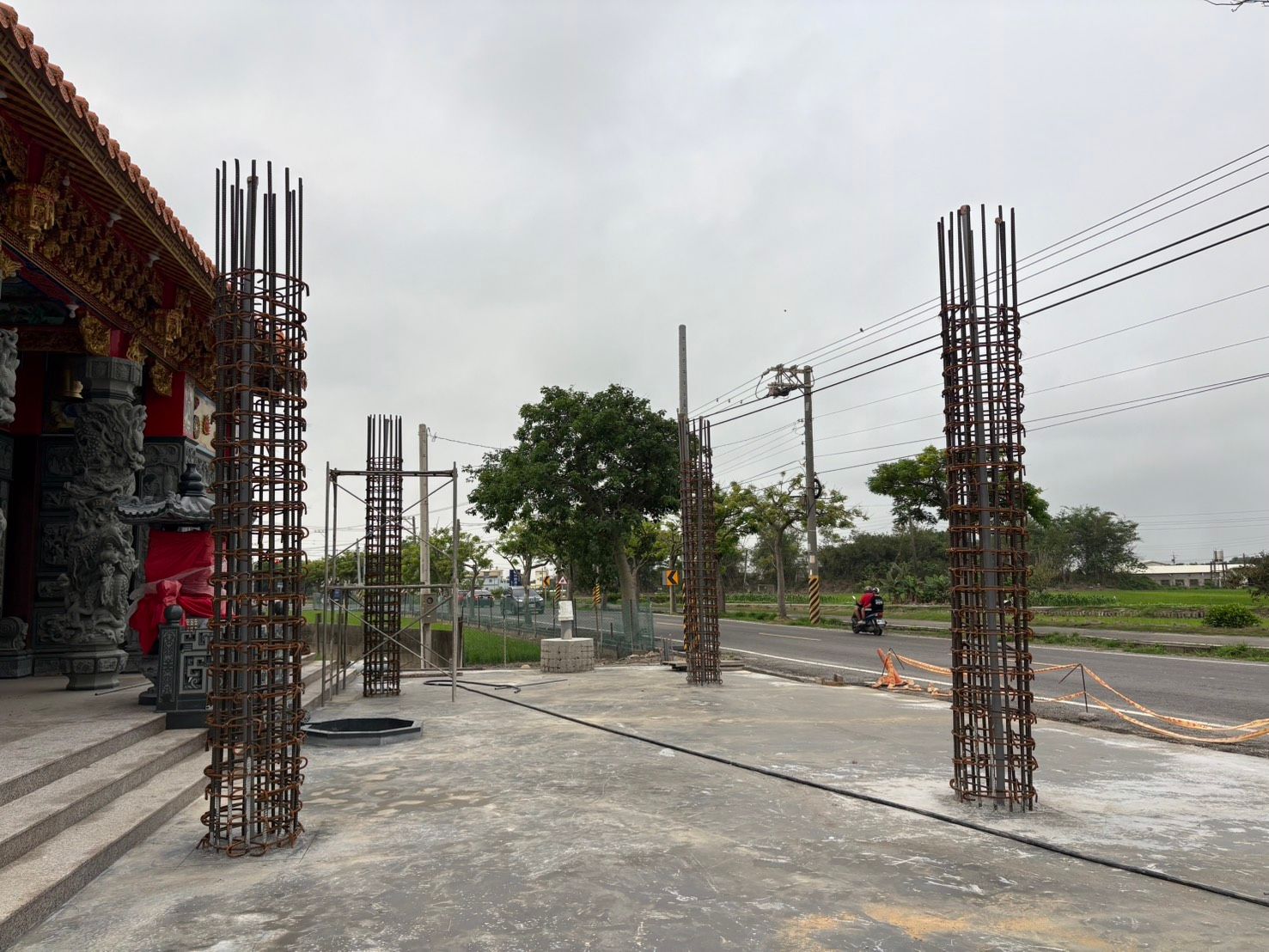 陰天下,建築工地上有混凝土柱、道路和一棵小樹。