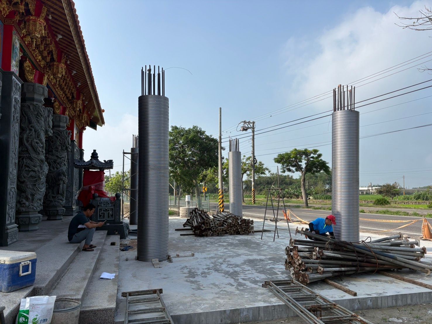 建築工地,混凝土柱、鋼筋和工人在建築物旁的鋪砌區域上作業。