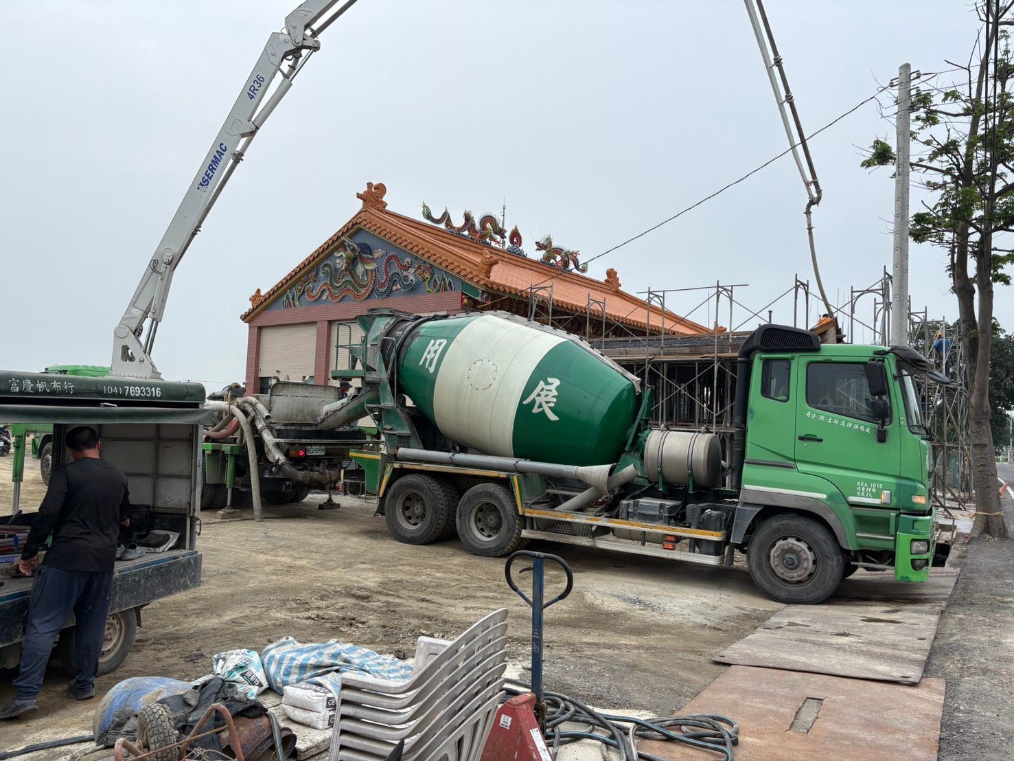 一輛綠色水泥攪拌車停在正在翻修的房屋旁的建築工地上。