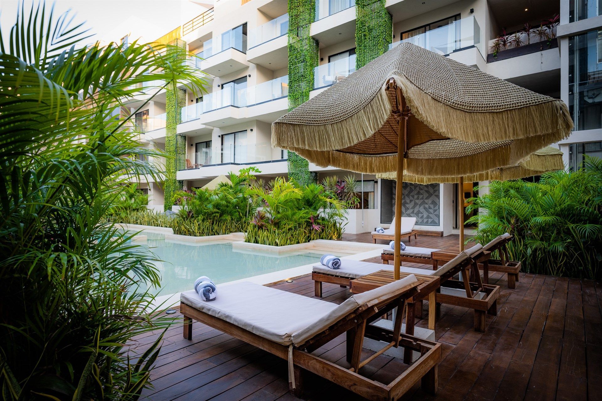 Una piscina con sillas y sombrillas frente a un edificio. Hotel Bakal Tulum