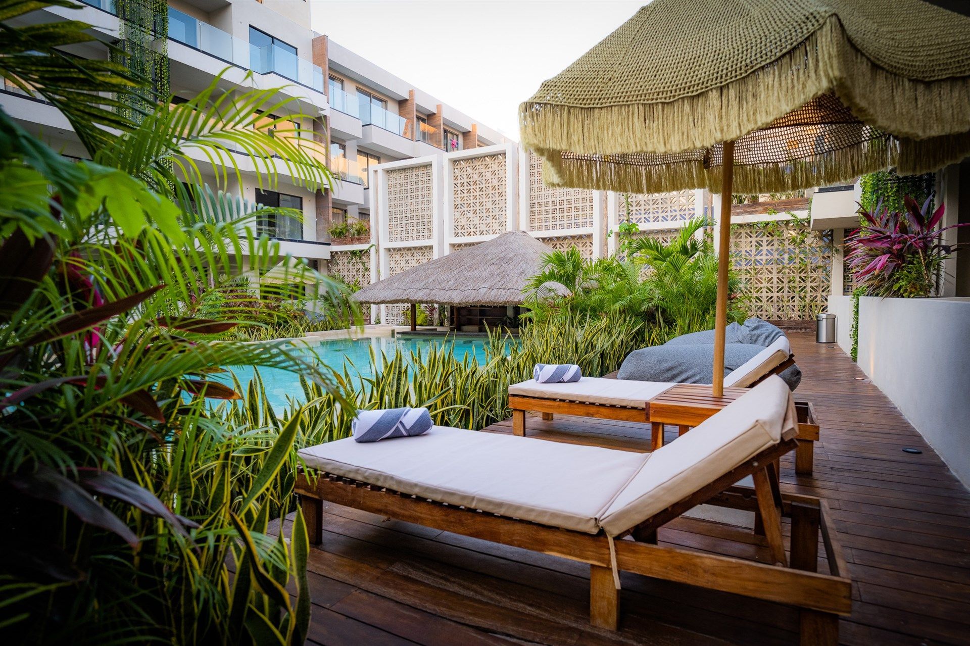 Un par de tumbonas bajo una sombrilla junto a una piscina. Hotel Bakal Tulum