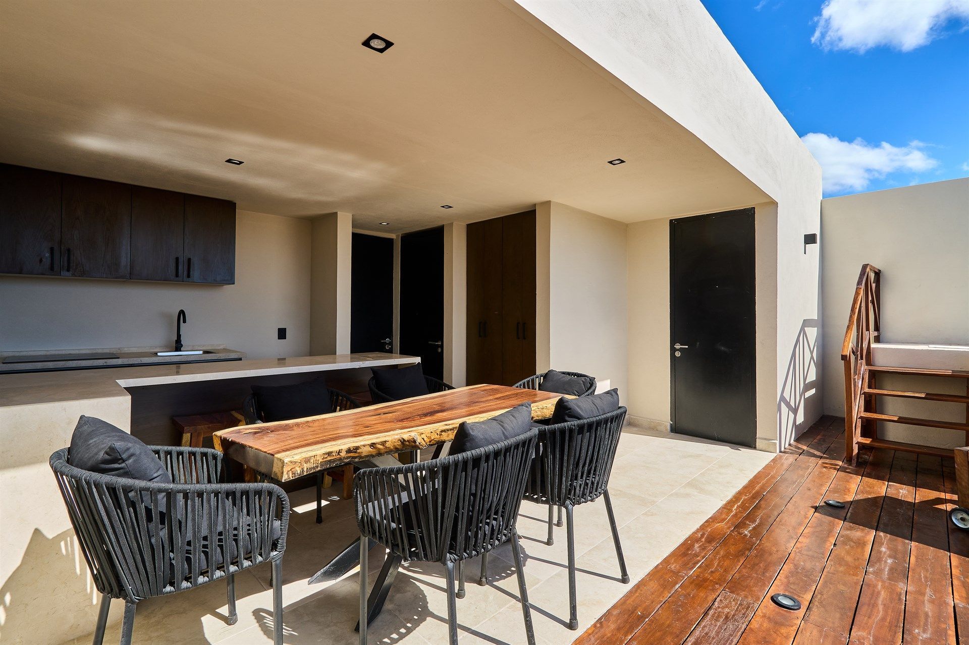 Una mesa y sillas de madera están ubicadas en un patio al lado de una cocina. Hotel Bakal Tulum