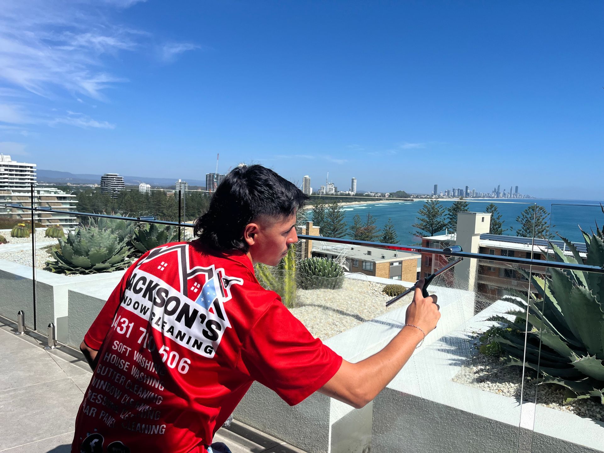 Person in Red Shirt Holding Phone, Filming a Coastal Landscape From a Rooftop — Jackson's Window Cleaning in Nerang, QLD