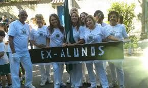 Um grupo de pessoas está de pé, uma ao lado da outra, segurando uma placa que diz ex-alunos.