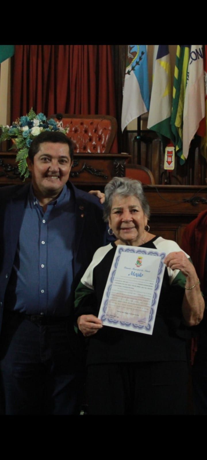 Um homem e uma mulher estão de pé, um ao lado do outro, segurando um certificado.
