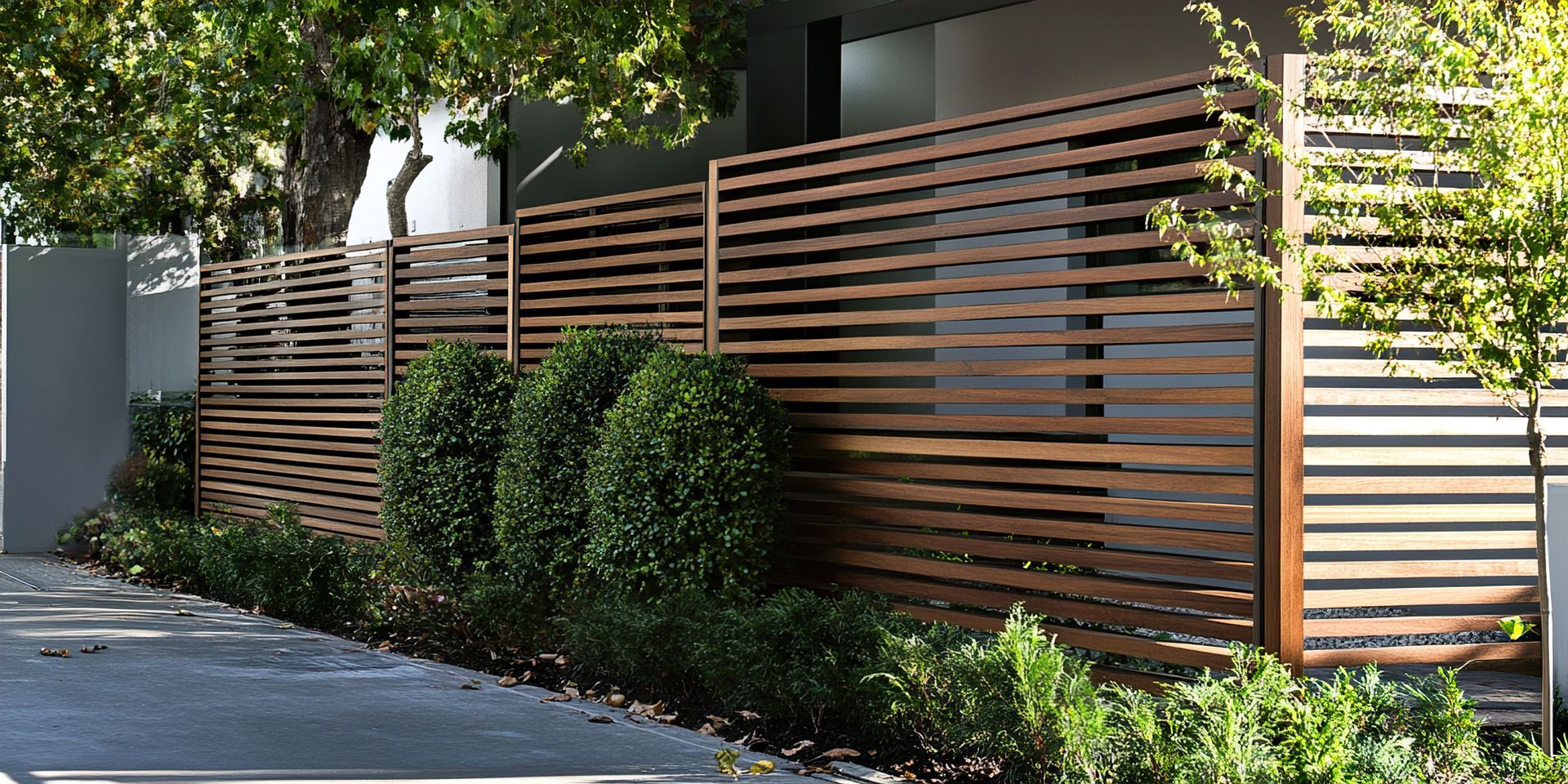 Wooden slat fence with lush green shrubs in front.