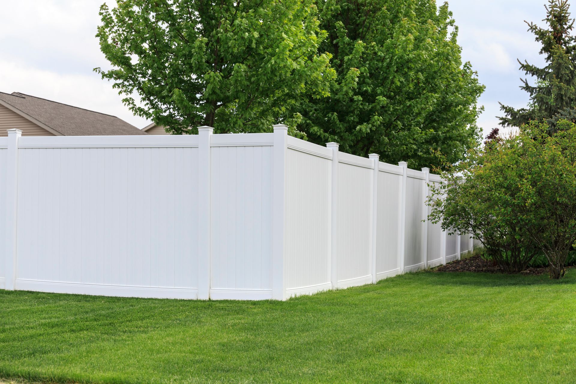 White vinyl fence in a grassy yard, with green trees in the background.