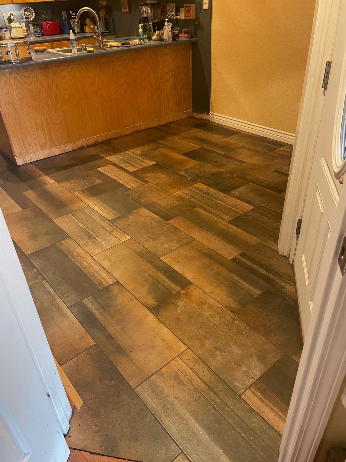 Wooden plank-style flooring in kitchen with wood cabinetry. A doorway is to the right.