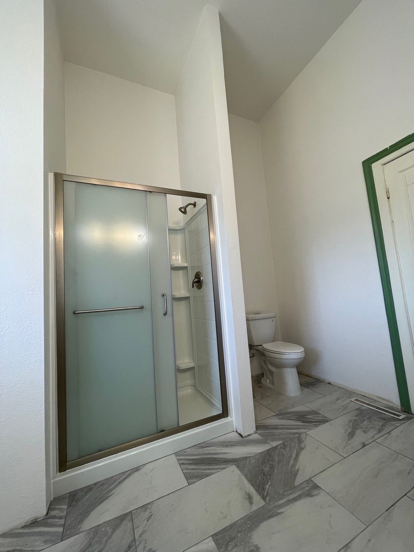 Bathroom with a frosted glass shower, toilet, and gray tiled floor.