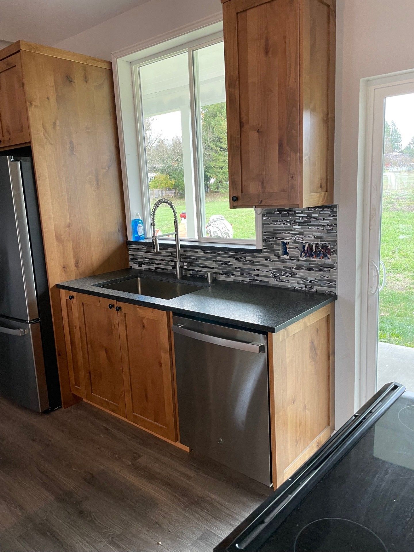 Kitchen with wooden cabinets, a sink, and a dishwasher, with a window overlooking a yard.