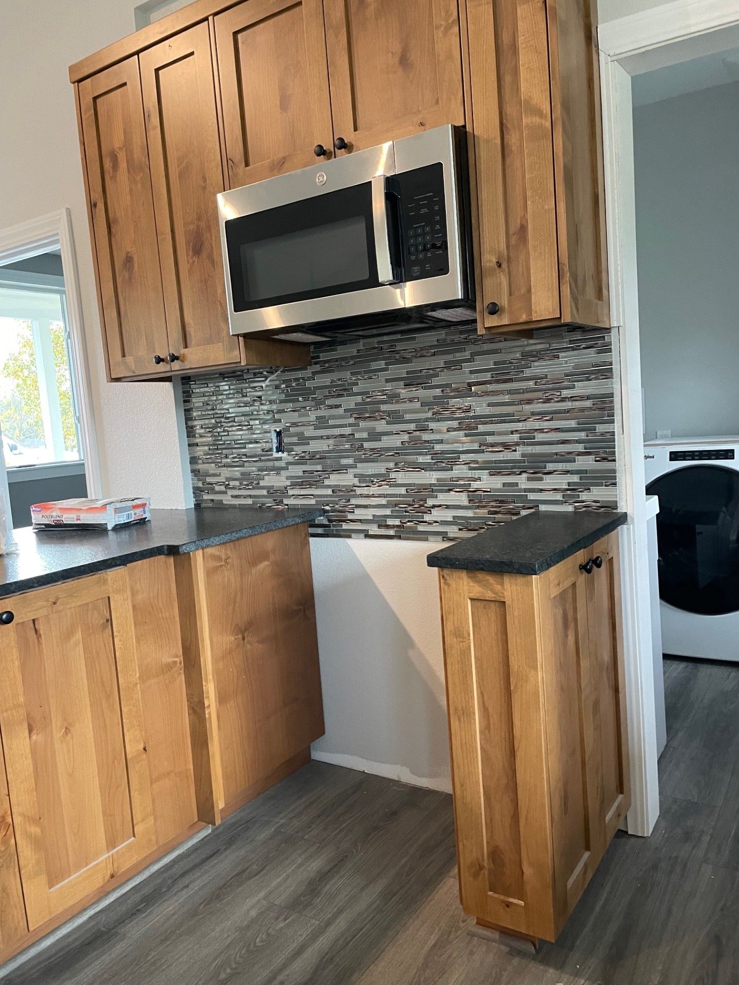 Kitchen with light wood cabinets, dark countertops, and microwave above a tiled backsplash.