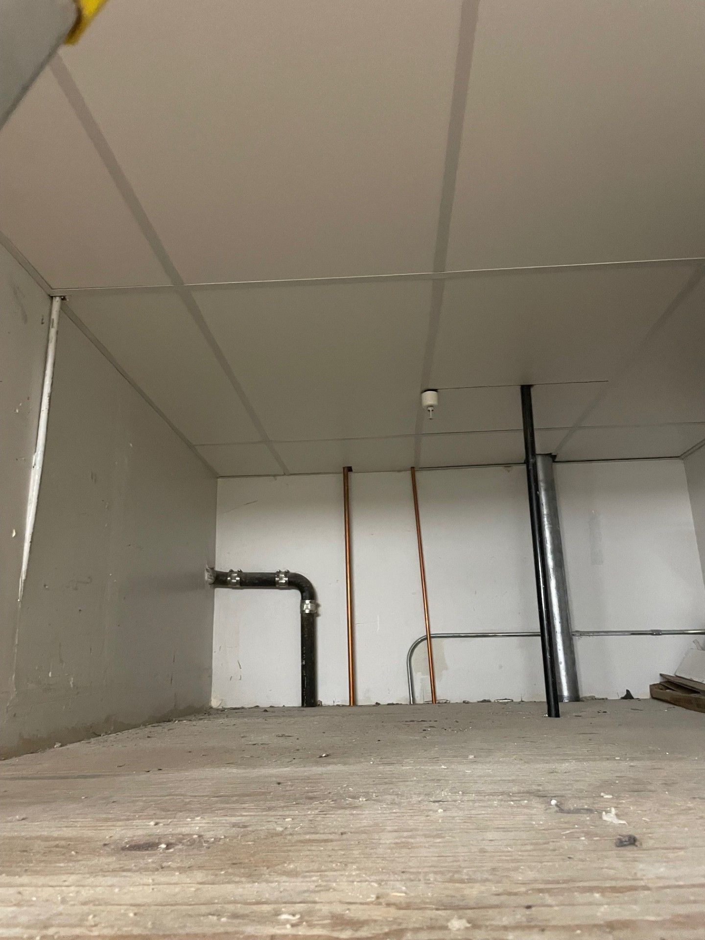 Empty room with white walls, ceiling, exposed pipes, and a concrete floor.