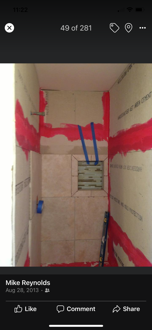 Shower stall with red waterproofing, tile, and blue plumbing.