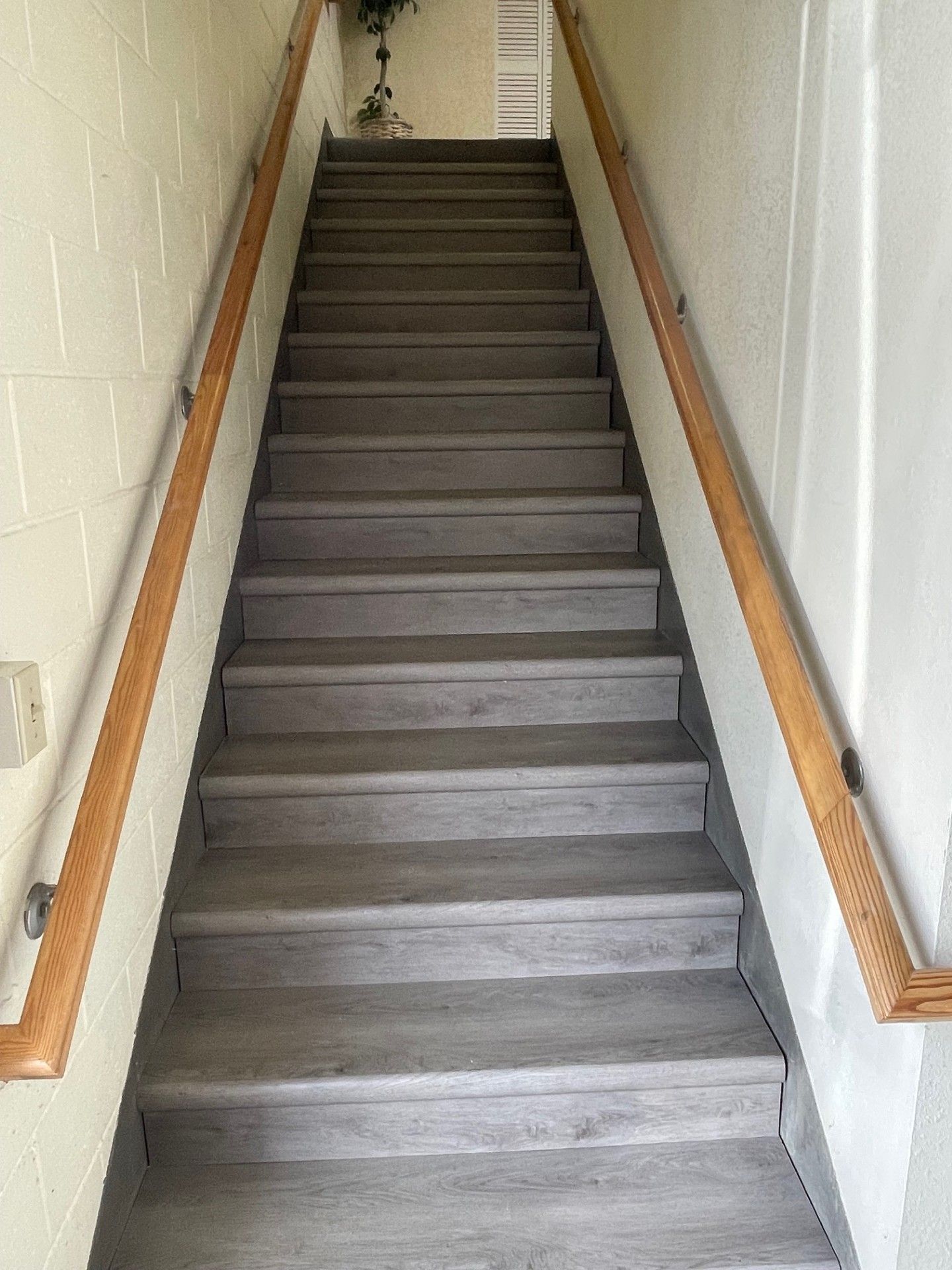 Staircase with gray steps, wooden handrails on both sides, leading upwards in a narrow hallway.