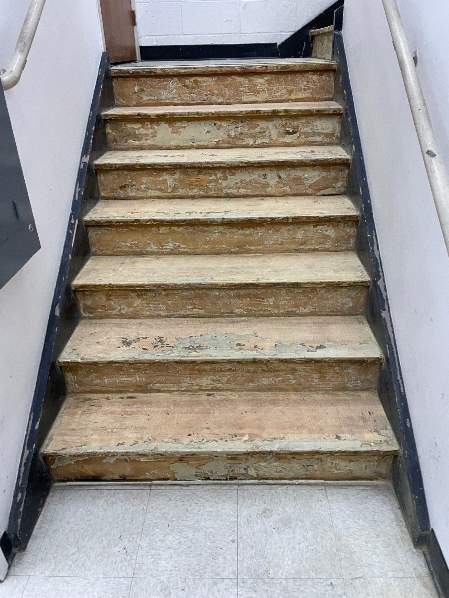 Staircase with worn, light-brown steps, black side rails, and a white wall on each side.