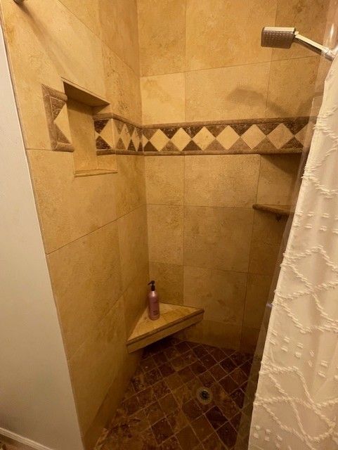 Tiled shower with corner seat and shelving, featuring a decorative border and a bottle on the seat.