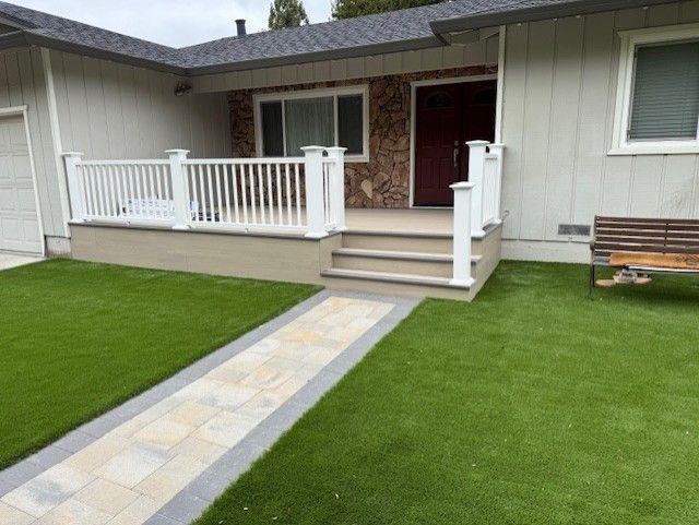 House exterior with walkway, porch, and white railing. Green lawn, beige siding, dark front door.