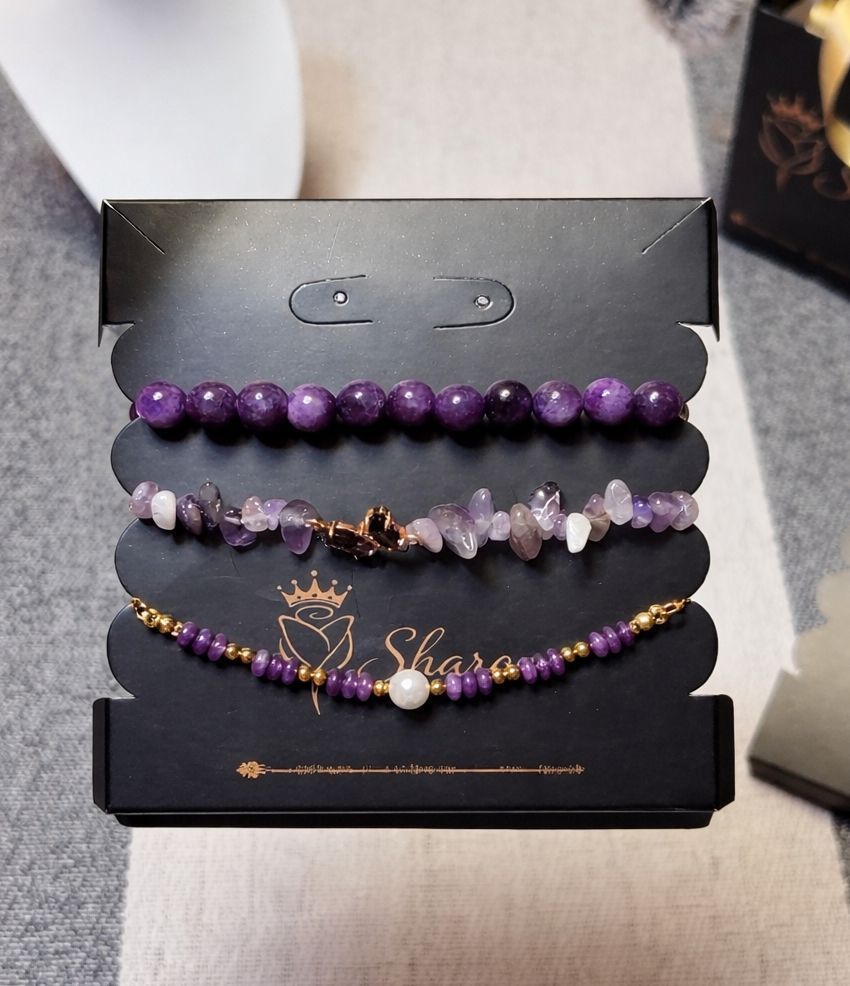 Tres pulseras de cuentas en tonos morados presentadas en una tarjeta negra con el logotipo de la marca.