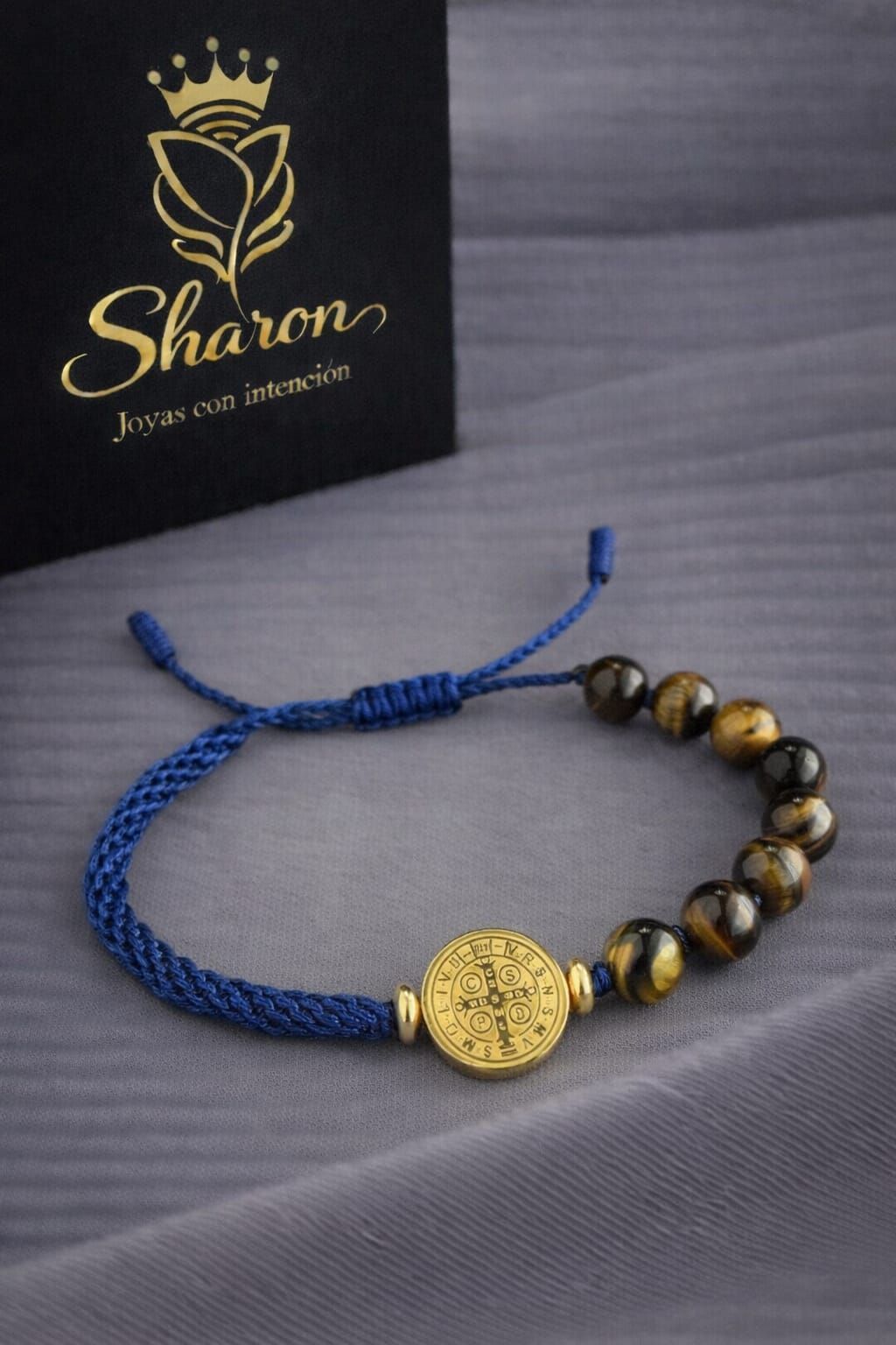 Una pulsera de cordón azul con cuentas de ojo de tigre y un medallón dorado