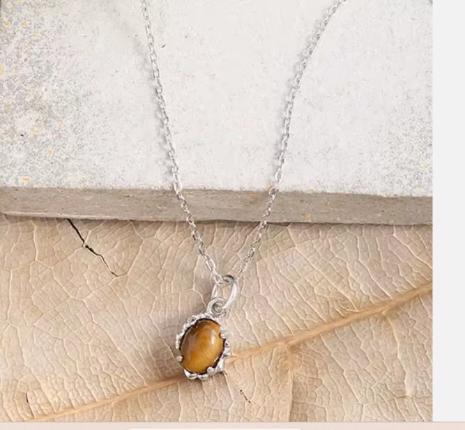 Un collar de plata con un pequeño colgante ovalado de ojo de tigre de color marrón dorado